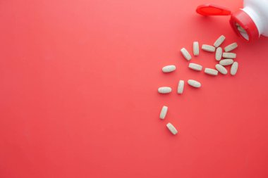  Kırmızı arka plana beyaz renkli tıbbi haplar dökülüyor. 