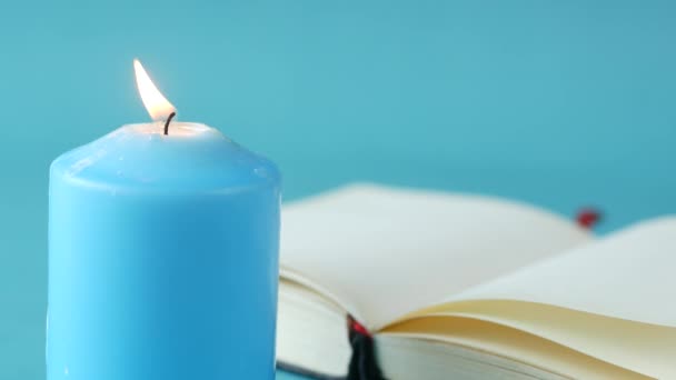 Свечи голубого цвета медленно сгорают и открывают книгу на столе — стоковое видео