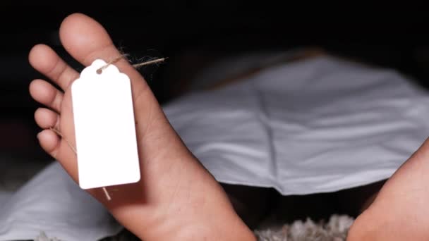 Le corps de l'homme mort avec une étiquette vierge sur les pieds sous un tissu blanc dans une morgue — Video