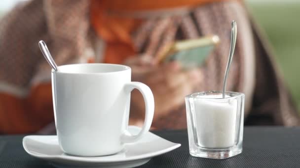 Coffee cup and sugar on table while women using smart phone in background — Stock Video