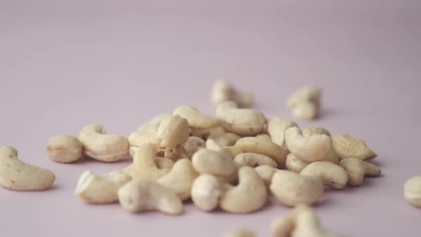 Slow motion av cashewnötter faller på ljusrosa bakgrund — Stockvideo