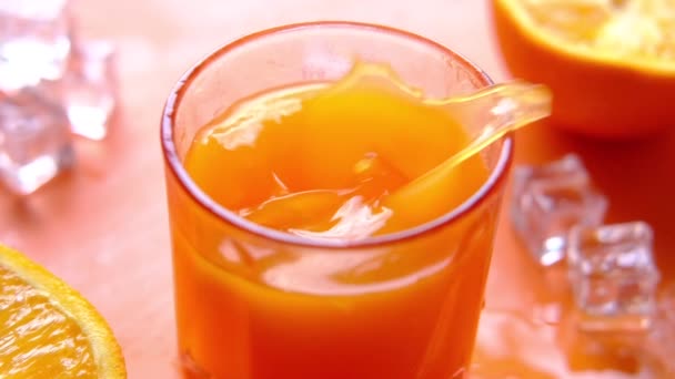 Câmera lenta de gotas de cubo de gelo em um copo de suco de laranja — Vídeo de Stock