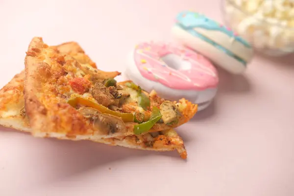Fetta di pizza al formaggio su un piatto, ciambelle e popcorn su rosa — Foto Stock
