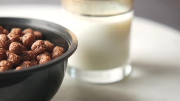 Close-up van chocolade cornflakes in een kom op en melk op tafel — Stockvideo