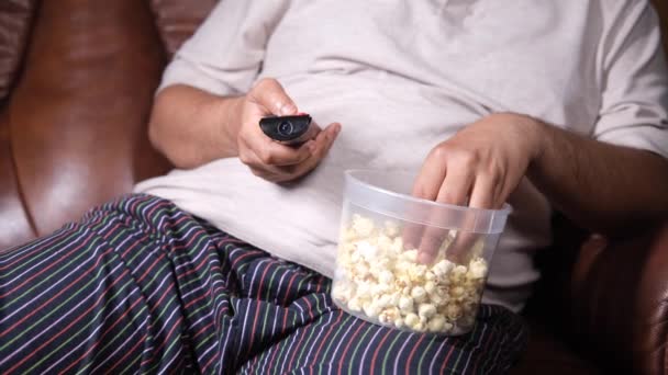 Um jovem gordo comendo pipocas e assistindo tv remoto — Vídeo de Stock