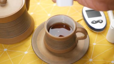  putting artificial sweetener in tea and a glucose meter on table 