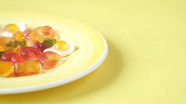 Gummy candies on a plate on yellow background . — Stockvideo