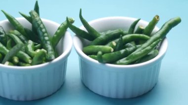 Masanın üzerindeki beyaz kasede yeşil biberi yakın. 