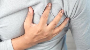 Genç adam kalp ağrısı çekiyor ve göğsünü eliyle tutuyor. .