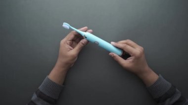  Elinde mavi renkli elektronik diş fırçası var. .