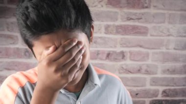 sad teenage boy covering his face sitting on sofa ,