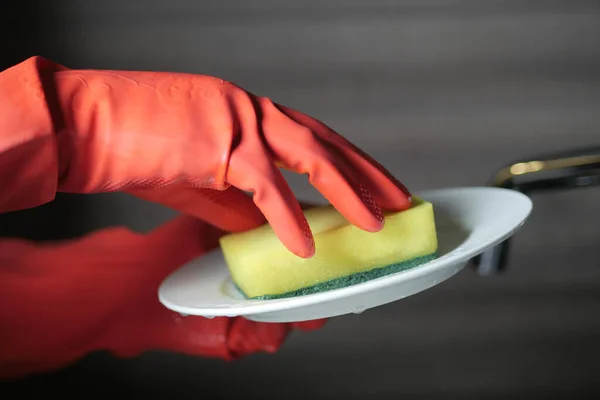 hand in rubber gloves cleaning a white plate with sponge ,