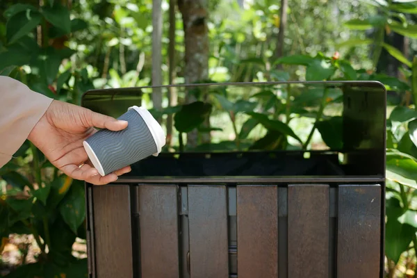 women hand throwing an empty paper coffee cup in the garbage trash or bin,