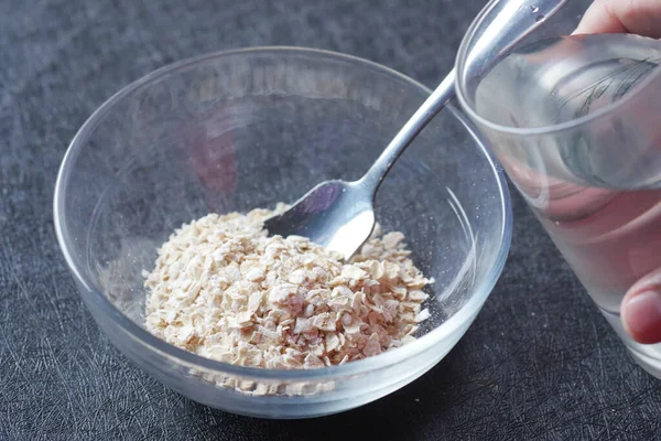 putting water in raw oats flakes in a bowl .