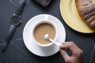 İnsan, kaşıkla kahve karıştırır.