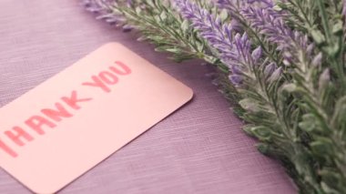 thank you message on sticky note and lavender flower on table .