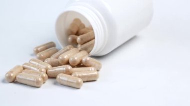 herbal medicine capsule spilling from a container on white .