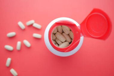 top view of pills spilling from a container on red ,