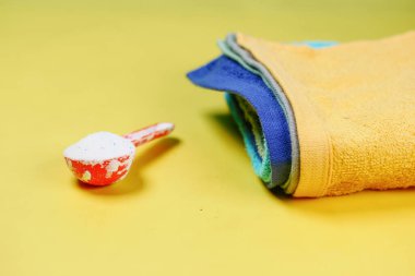 Plastik kaşıkta yıkama tozu ve sarı arka planda renkli giysiler. .