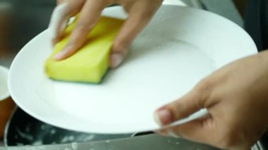 Kadınlar beyaz bir tabağı süngerle yıkıyor. ,