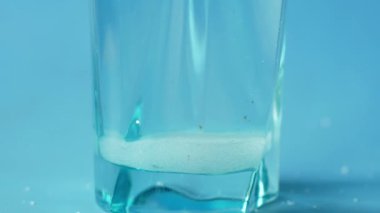 Mavi arkaplanda bir bardak suya beyaz şeker dökerek ,