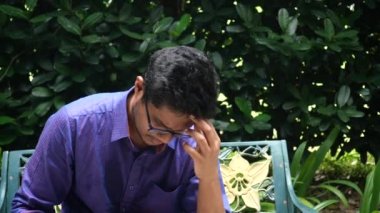 Genç adam baş ağrısı çekiyor, parkta bir bankta oturuyor. ,