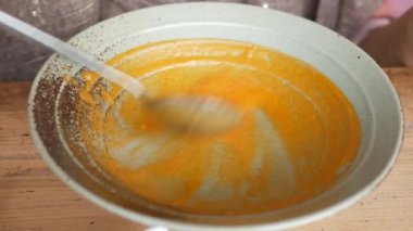 stirring a bowl of yellow vegetables soup .