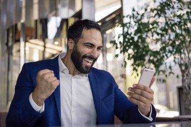 Mutlu duygusal iş adamı elinde cep telefonu ile ofiste iyi haberler okuyor. Genç yakışıklı tüccar kutlama başarısı 