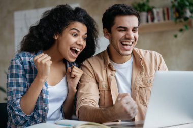 Dizüstü bilgisayar kullanan, satışlarla alışveriş yapan, dijital ekrana bakarak oyun oynayan aşırı neşeli birkaç arkadaş. Mutlu Afrikalı Amerikalı kadın ve Hintli erkek online piyango zaferini kazandı.