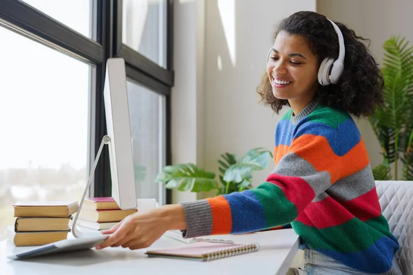 Gülümseyen Afrikalı Amerikalı serbest çalışan evde çalışan bir bilgisayar kullanıyor. Kablosuz kulaklık takan, iş yerinde müzik dinleyen mutlu bir kadın. 