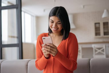 Sıradan kıyafetler giyen Afro-Amerikalı bir kadın akıllı telefon mesajları tutuyor, internette iletişim kuruyor ve evde oturuyor. Gülümseyen hippi kadın internetten mobil uygulama alışverişi yapıyor.
