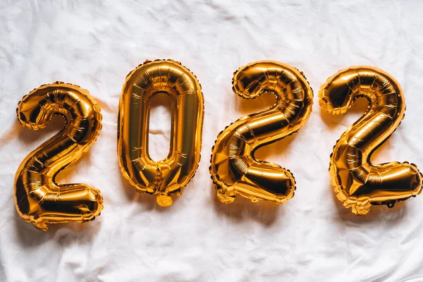 2022 golden foil balloons on bed. Happy new year, celebrating festive concept. Top horizontal banner view copyspace. Holiday background Happy New Year 2022. close-up Numbers of year 2022 on white.