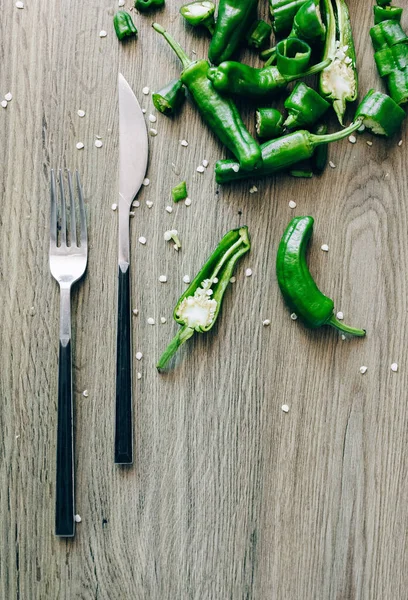 Green Chilli peppers Beside Silver Fork and Knife on brown wooden Table Board