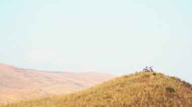 Kırmızı bisiklet tepede duruyor. Bisikletçi ve manzaralı dağlar yok. Arka planda vahşi doğa var.