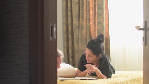 Молодые Мамы Нянечки Помогают Мальчику Домашними Тетрадями Лежащими Кровати Спальне — стоковое видео