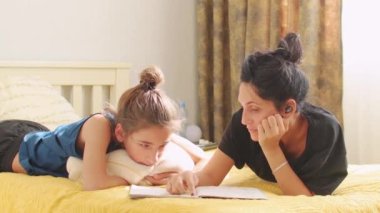 Genç anne ya da bebek bakıcısı yatağa uzanmış ve çocuğa ödevi olan okul defterini okumasında yardım etmiş. Yatak odasında oturmuş. Şefkatli anne anaokulu çocuğuna dersi açıklar. Annem oğluyla evde vakit geçiriyor.