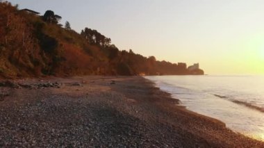 Dişi insan gün batımında sakin deniz manzarasıyla rahatlarken deniz kenarında kayalık sahilde tek başına oturur. Yalnızlık konsepti ve refah