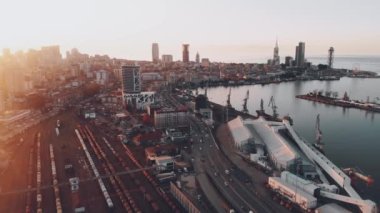 Demiryolu ve otoyol ile Batumi 'de geriye dönük hava manzaralı nakliye; liman panorama ve kıyı şeridi boyunca ufuk çizgileri üzerinde günbatımı ile gezinti. Georgia mı? Kafkaslar 4k