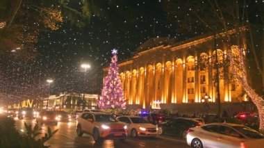 Gürcistan 'ın başkenti Tiflis' teki Rustaveli Bulvarı 'nda yoğun saatlerde trafikte duran durağan zaman aralıklı arabalar ve parlamentonun arka planında Xmas ağacı bulunuyor.