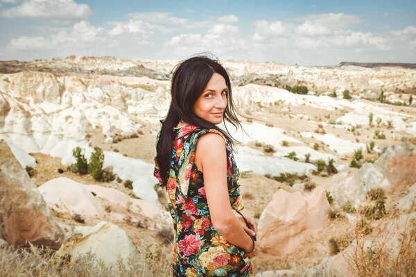 Young attractive smiling brunette woman in beautiful flower dress joyfully pose travel photo looking to camera with beautiful nature landscape background