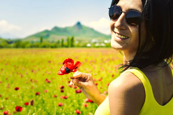若いです幸せなCaucasianブルネット女性を保持シングルケシの花とフィールドで晴れた日を楽しむ — ストック写真
