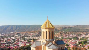 Güneşli bir günde Tiflis katedralinin dış yüzeyi ile şehir panoramasını tarıyoruz. Tiflis 'in Kutsal Üçlü Katedrali' nin hava görüntüsü. Gün batımı İHA görüntüleri.