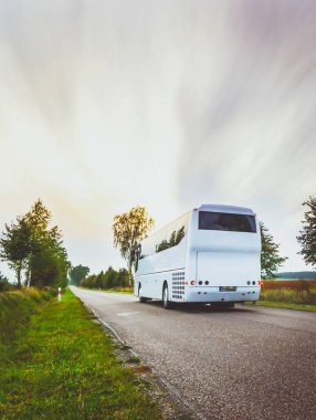 Gezintide kırsal yolda hareket halindeki beyaz otobüs insanları Avrupa 'daki turizm beldesine götürüyor