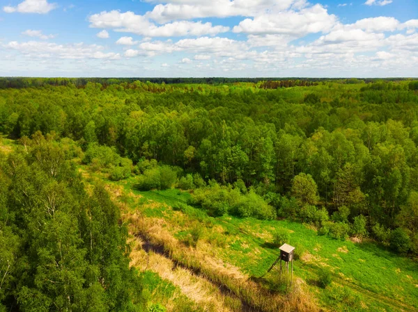 Wide aerial view wooden hunting tower in sunny day. Aerial view from above big fields of farm land and one lonely wooden hunting tower