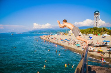 Batumi, Gürcistan - 4 Ağustos 2022: Beyaz turist erkek sıcak yaz gününde Batumi rıhtımından deniz suyuna atlıyor. Georgia 'da Karadeniz kıyısında tatil. Kafkaslar seyahat eder