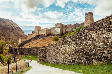 Dişi turist bulutlu bir günde üzerinde kuleler bulunan dev Khertvisi kale duvarının yanında duruyor. Seyahat telif uzayı arkaplanı.