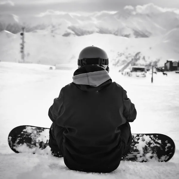 Male man snowboarder sit enjoy inter mountain panorama in ski resort alone in majestic mountains.