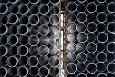 İnşaat alanında kullanılan gri plastik kanalizasyon borularının arka planı. Plastik drenaj borusunun dokusu ve deseni. Tüplerin içinden ışık.