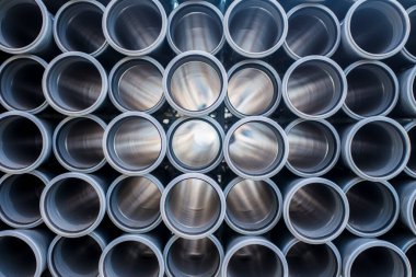 İnşaat alanında kullanılan gri plastik kanalizasyon borularının arka planı. Plastik drenaj borusunun dokusu ve deseni. Tüplerin içinden ışık.