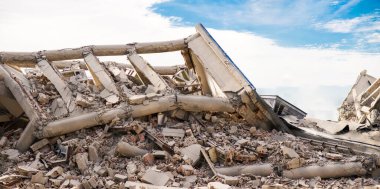 Çökmüş beton endüstriyel çok katlı binanın panoramatik görüntüsü. Enkaz, toz ve hasarlı evlerle dolu felaket sahnesi.